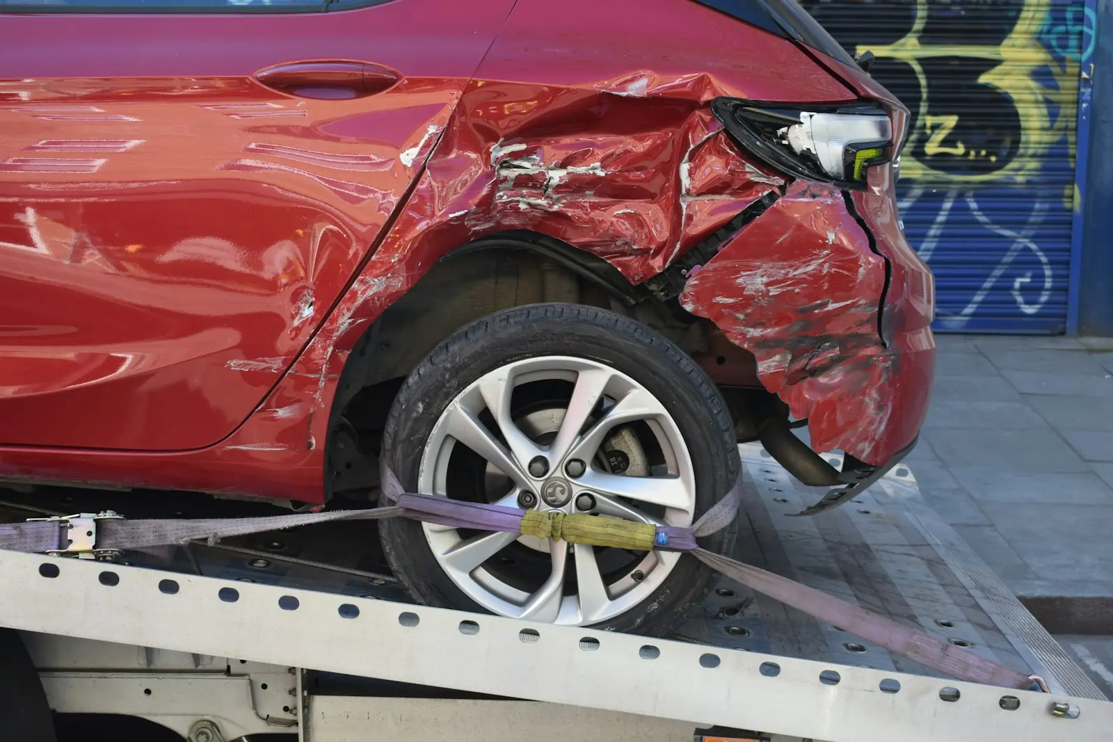 Damaged red car strapped on a flatbed tow truck