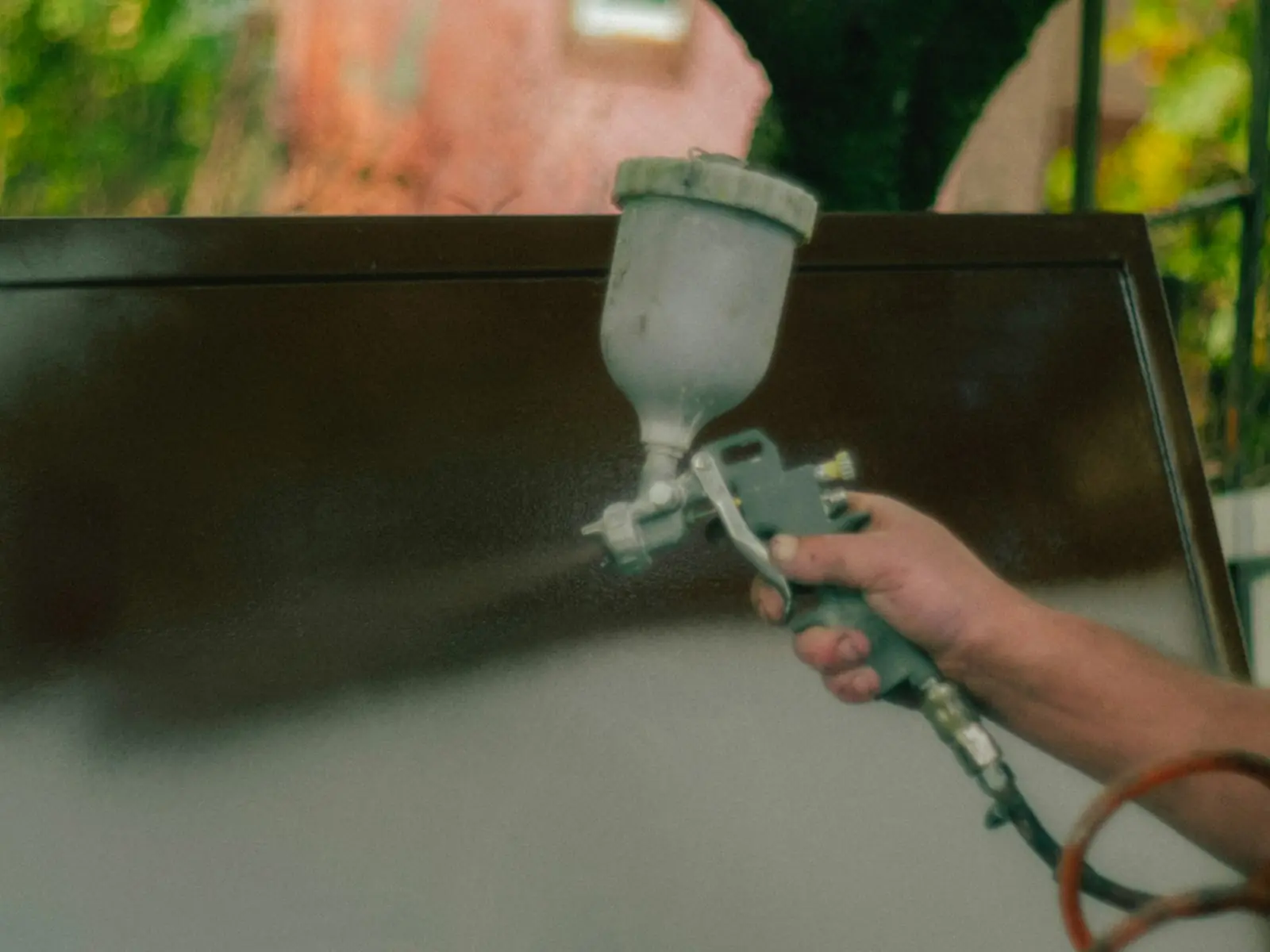 Painter's hand holding a spray gun applying paint to a panel