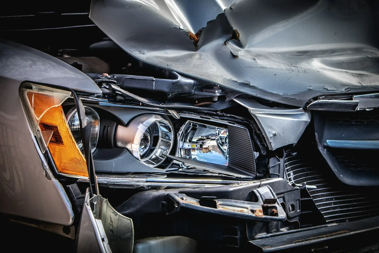 Silver car with a crushed hood and broken headlight after a front-end collision